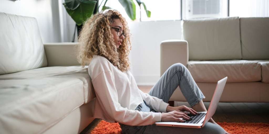 Ways to be an entrepreneur: Female with curly hair diligently working on her laptop in a modern living room setting.
