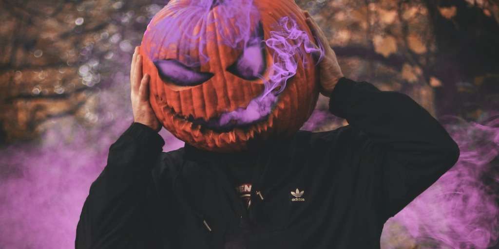 A man celebrating SA Halloween with a pumpkin on his head, SA celebrate Halloween, surrounded by eerie purple smoke.