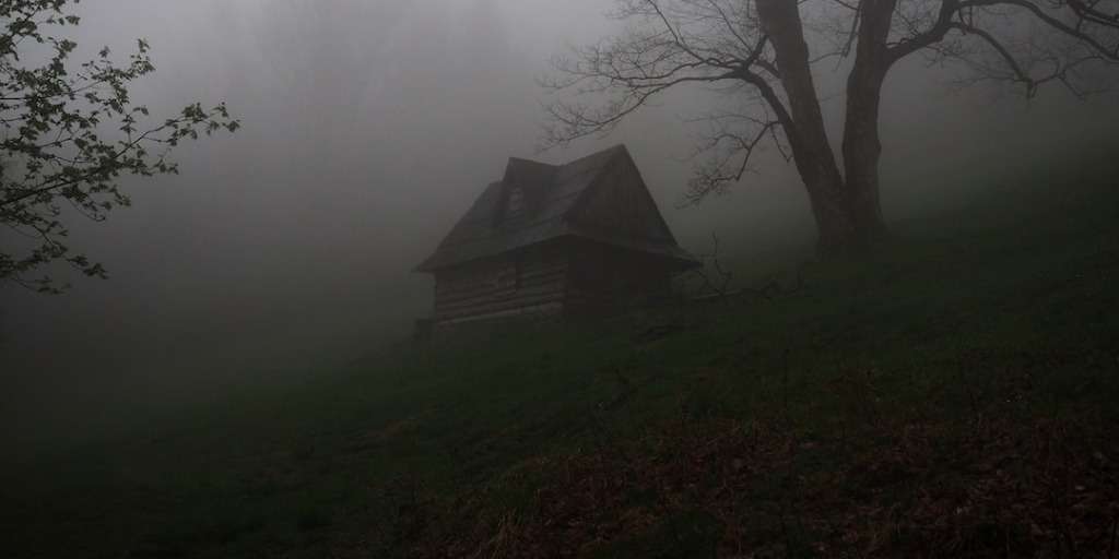 A foggy landscape with an eerie lone house amidst bare trees, capturing the essence of the Best Halloween Movies atmosphere.