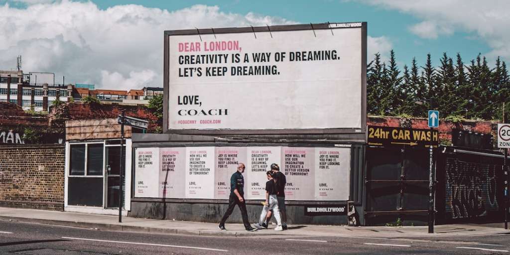Outdoor advertisement in London encouraging creativity, alongside a car wash with pedestrians passing by, demonstrating effective urban ad placement.