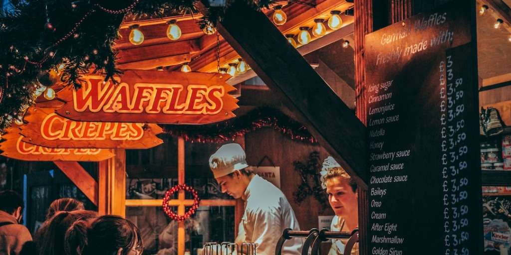Christmas market stall with waffles and crepes, glowing lights, epitomizes Best Christmas Market Finds.