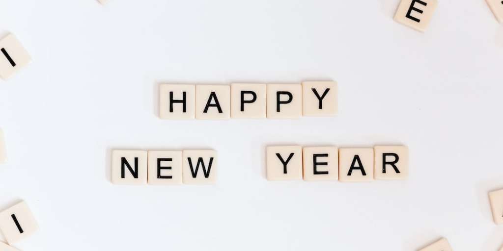 Scrabble tiles spell out 'HAPPY NEW YEAR' against a pale background, symbolizing the New Year's ritual that guarantees success in 2024.
