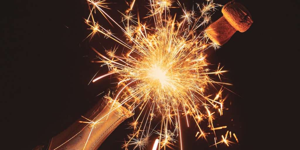 Champagne bottle with sparkling fireworks erupting, celebrating 'New Year, New You' in a festive explosion.