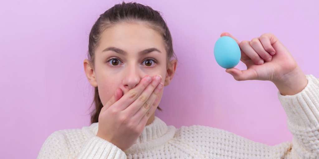 Surprised young woman with an age-old home remedy, holding a blue egg-shaped object.