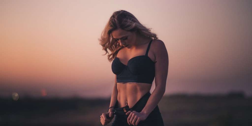 Woman fastening jeans after weight loss in just 7 days, showcasing a slim silhouette at dusk.