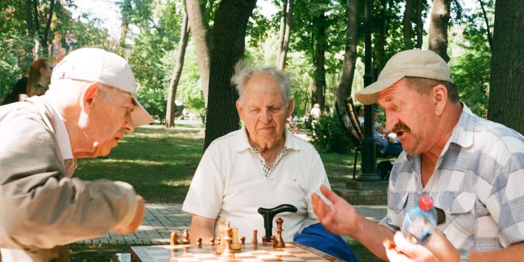 Elderly men playing chess in a park, enjoying social interaction, a Simple Trick Adds Years to Your Life.