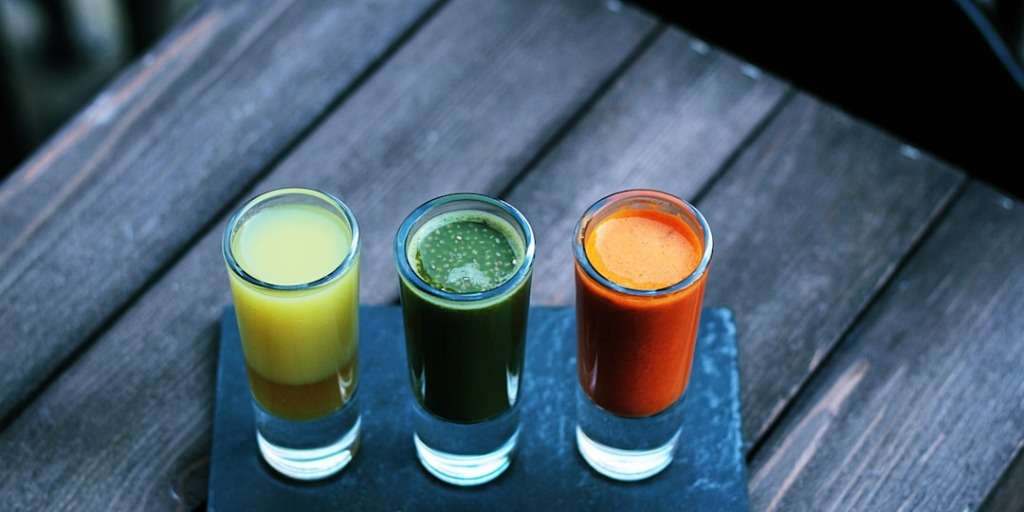 Three colorful health drinks on a wooden table, potentially representing weight loss shots.