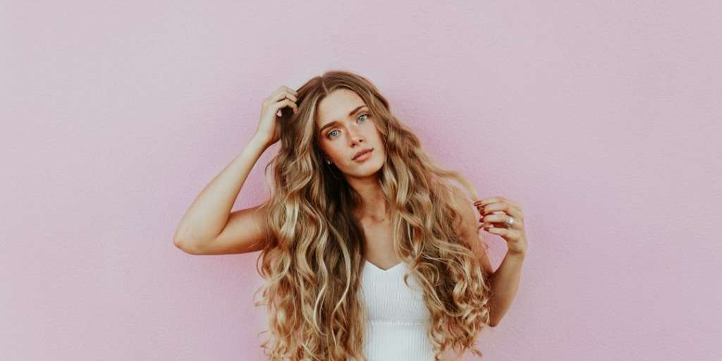 Woman with wavy blonde hair against a pink background, exemplifying our Hair Colour Guide.