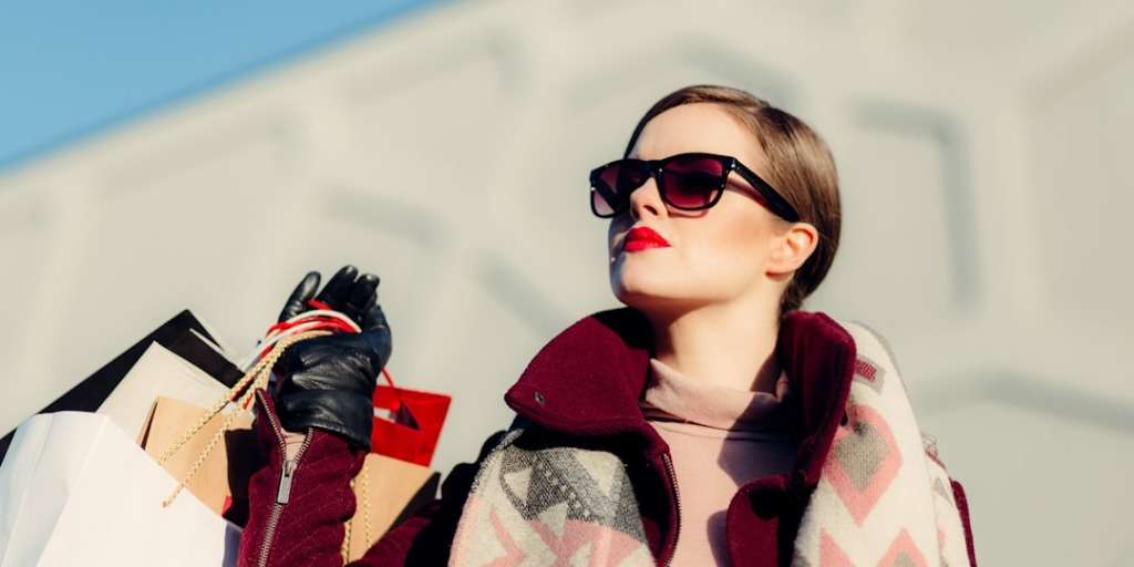 Woman with sunglasses and chic attire holds shopping bags, embodying the keyphrase 'Avoid Overshopping'.