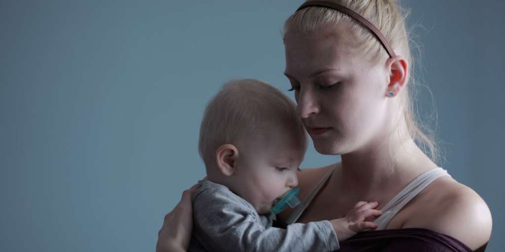 Stressed mother holding baby, emphasizing the importance of Self-Compassion After Birth for maternal well-being.