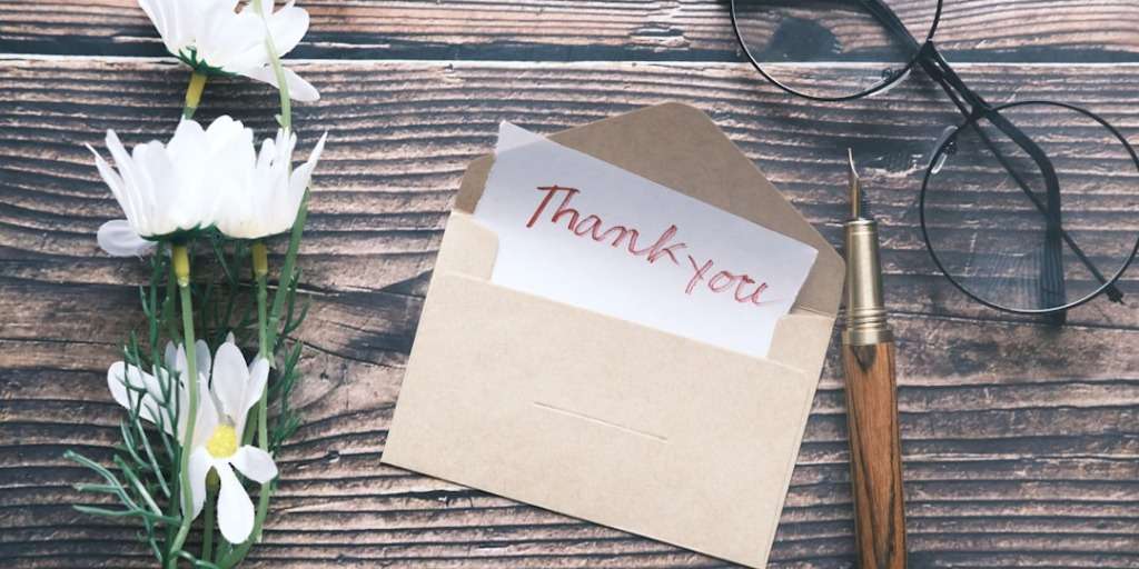 An "Appreciation" note: Thank you card with a pen and glasses on a wooden table alongside white flowers.