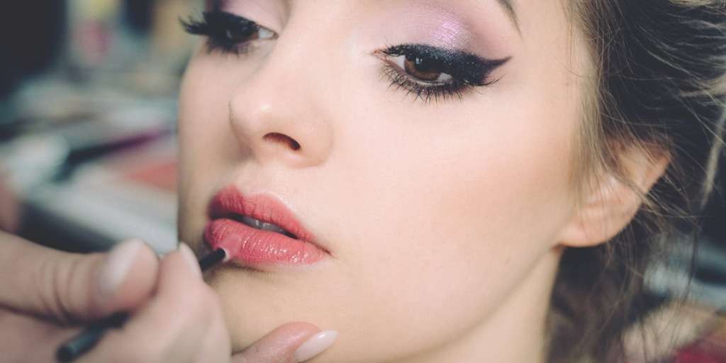 Woman receiving makeup application highlighting the best way to do your makeup with dramatic eyes and glossy lips.