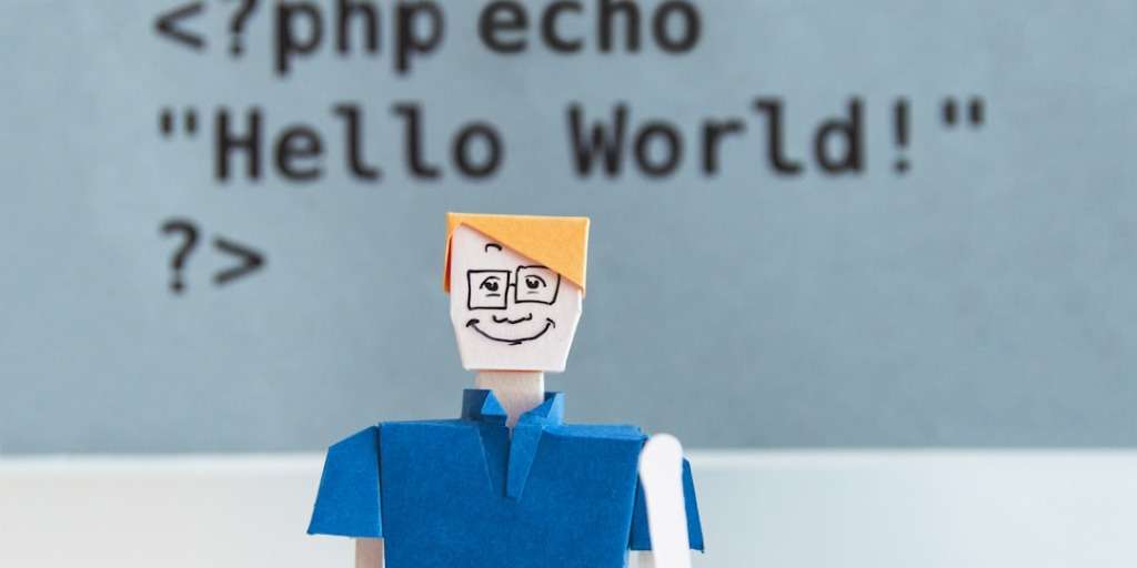 A paper figure of a Software Developer, symbolized by a "Hello World" PHP code snippet for WordPress.