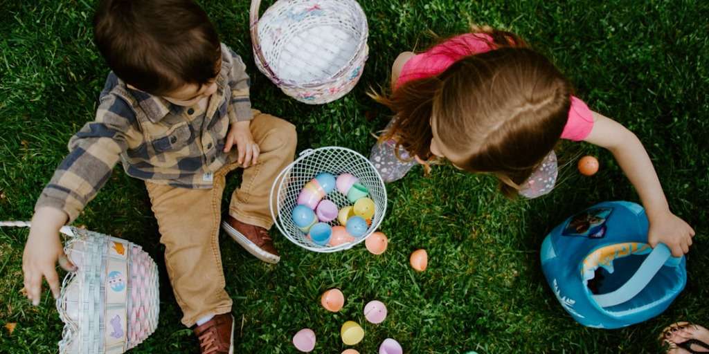 Two children gathering colorful eggs into baskets on a lawn, making Easter fun for kids.