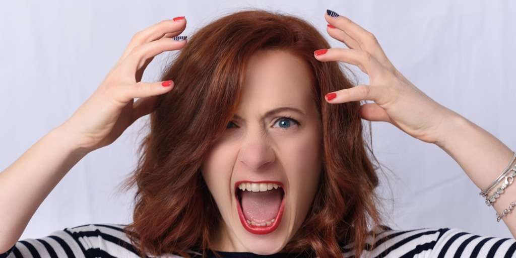 A woman with her hands in her hair, mouth open wide, unable to bottle emotions inside.