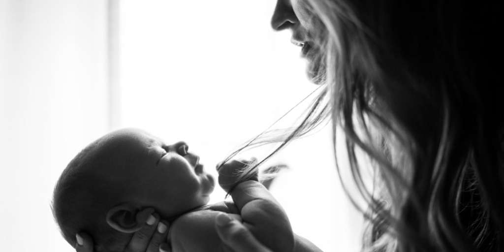 Mother comforting her infant, depicting what to do when your baby is teething, a tender moment in black and white.