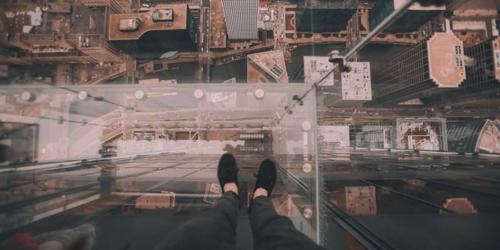 Person standing on a glass floor, overlooking a bustling city below, captures "Reveal Your Deepest Fear" theme.