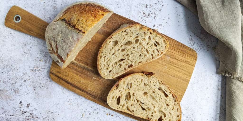 Best Sourdough Recipe: Freshly sliced sourdough bread on a wooden cutting board, rustic kitchen backdrop.