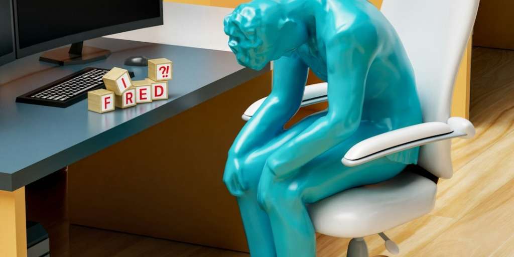 A person feeling dejected at work due to being retrenched because of AI, with blocks spelling 'Fired'.