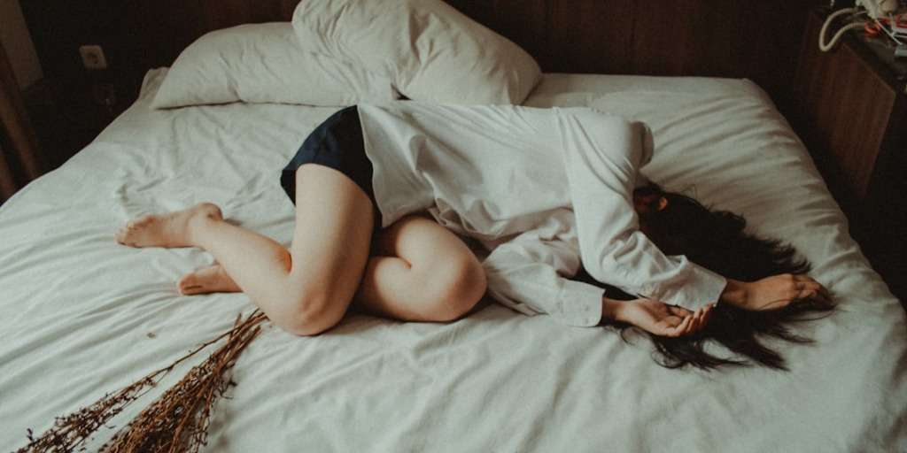 Person sleeping peacefully in a dark, quiet bedroom with a comfortable mattress and pillows, representing healthy sleep habits and the concept of catching up on sleep.